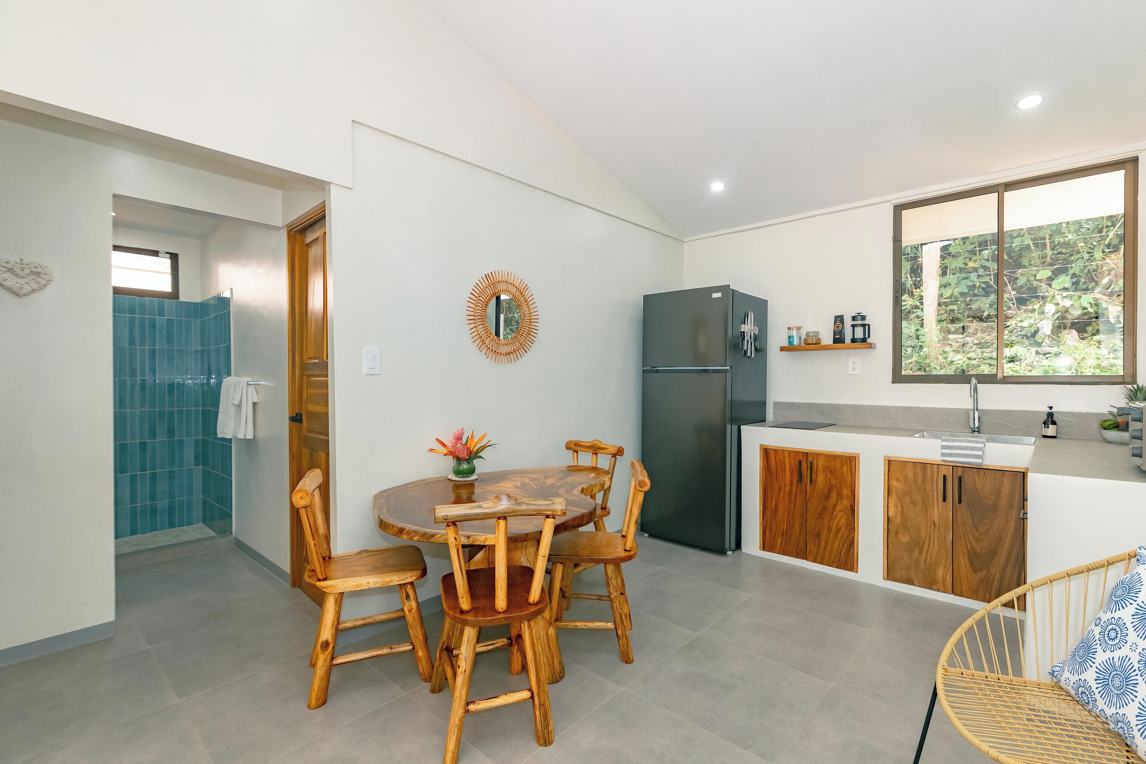 A modern kitchen with a dining area, wooden chairs, a round table, and a refrigerator.
