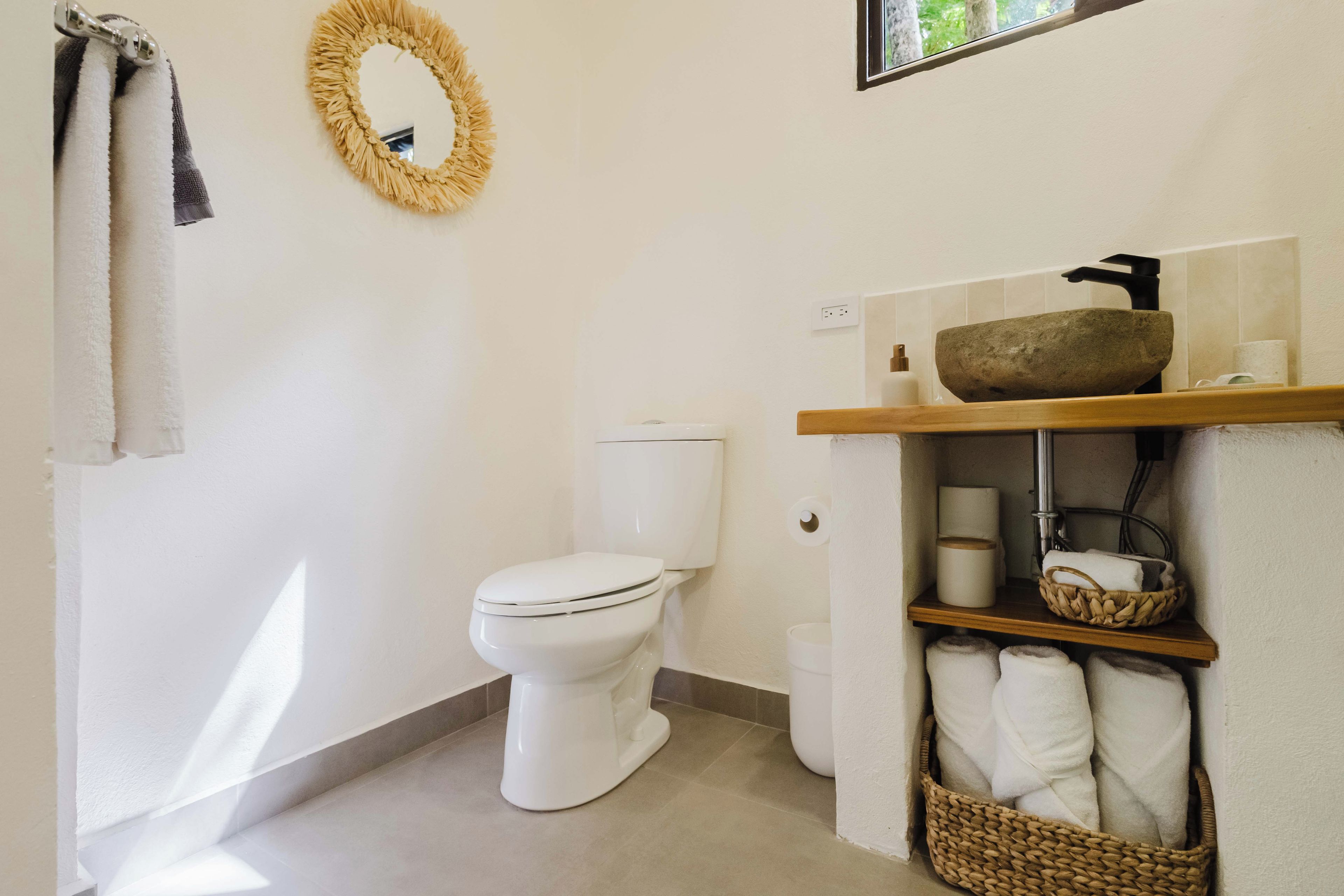 A bathroom with a toilet, a sink with a stone basin, and a towel rack with towels.