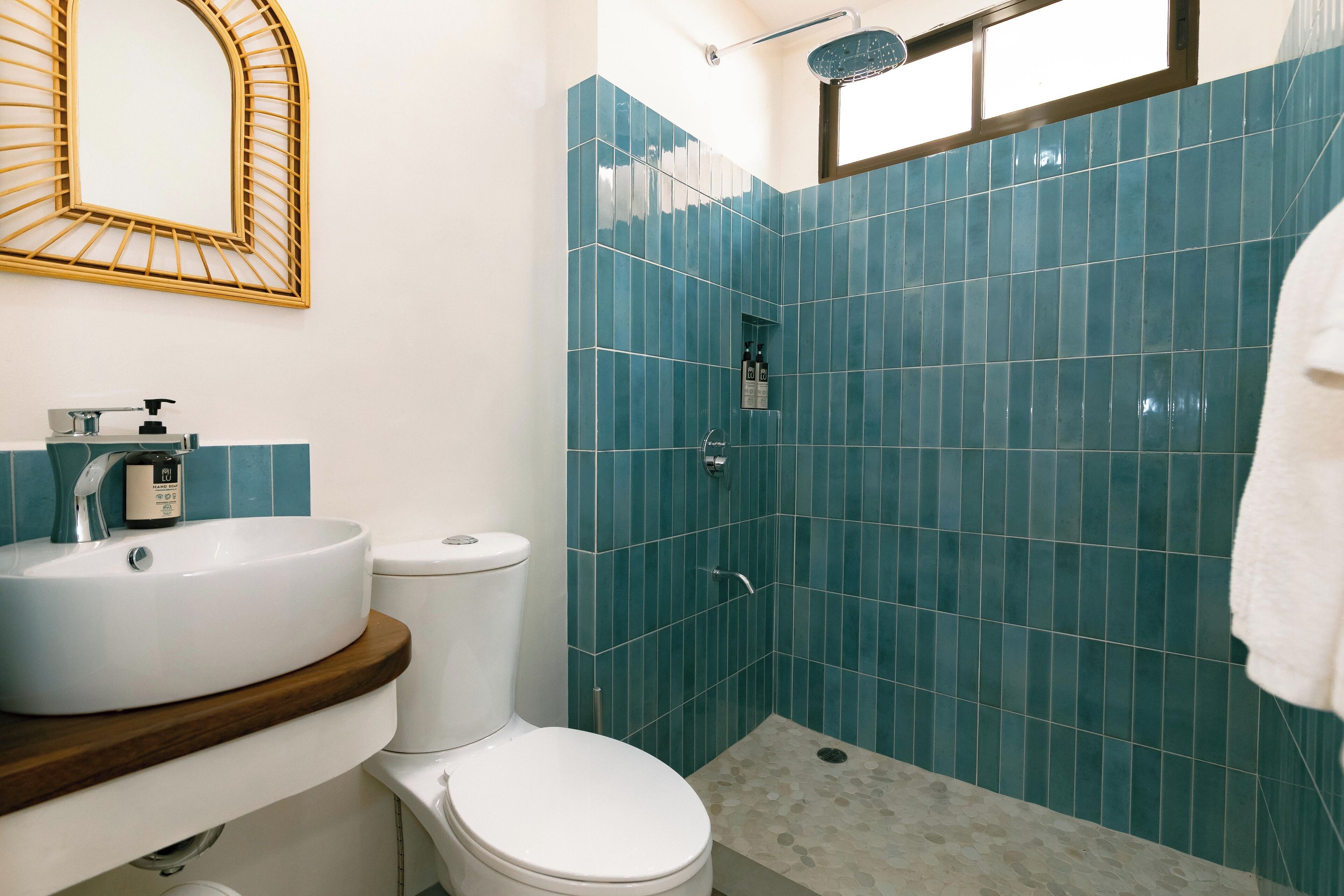A bathroom with a white toilet, a sink with a wooden countertop, and a shower with blue tiles.