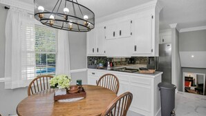 Una cocina moderna con armarios blancos, una mesa de comedor con sillas y una araña.