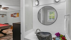 Un baño con un espejo redondo, un lavabo de piedra y un ventanal pequeño.