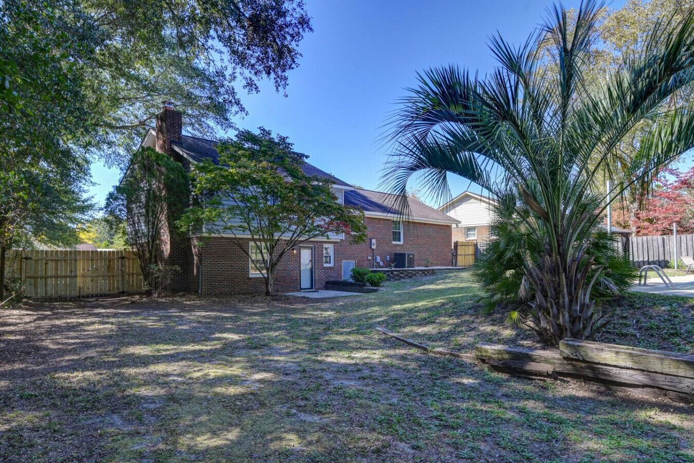 Un patio trasero residencial con una casa de ladrillo, cerca de madera y una palmera.