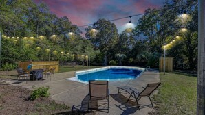 Un patio trasero con piscina, mobiliario exterior e iluminación colgante.