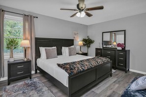 A modern bedroom with a bed, bedside tables, a dresser, a ceiling fan, and a large window with curtains. - Lexington Leisure House- 4BR w/ Pool & Games (Lexington)
