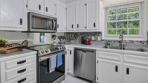 Una cocina moderna con armarios blancos, electrodomésticos de acero inoxidable y un ventanal con vistas al verdor.