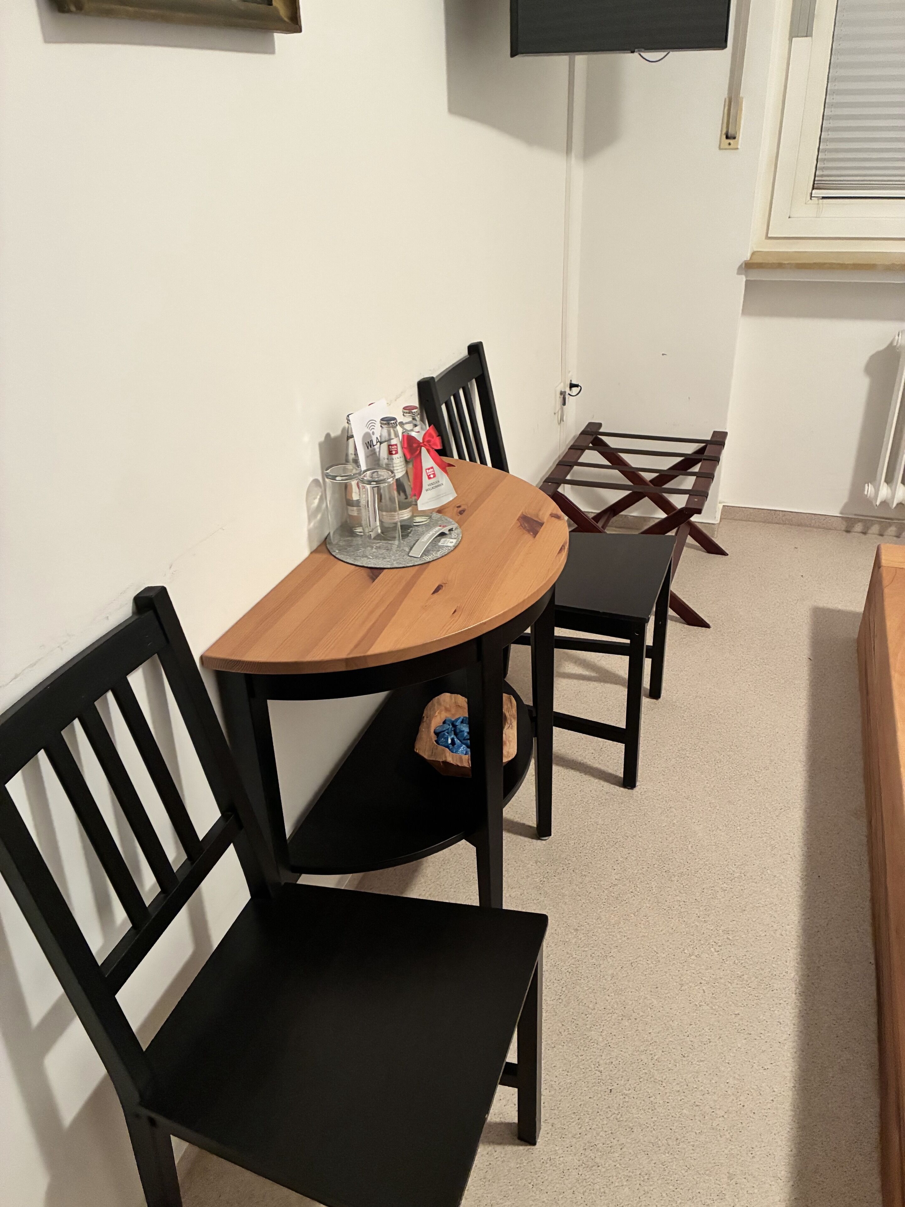 A dining area with a round wooden table, black chairs, and a TV mounted on the wall.