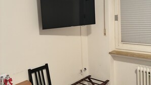 A room with a mounted TV, a wooden table with chairs, a radiator, and a window with blinds. - Das Gerhards (Wolfhagen)