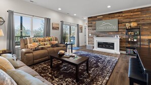 A modern living room with a fireplace, a sofa, a coffee table, and a bookshelf. - Chatt Vistas|NatPrks|4bdr|Theater|Hot Tub|Sleeps15+ (Fairview)