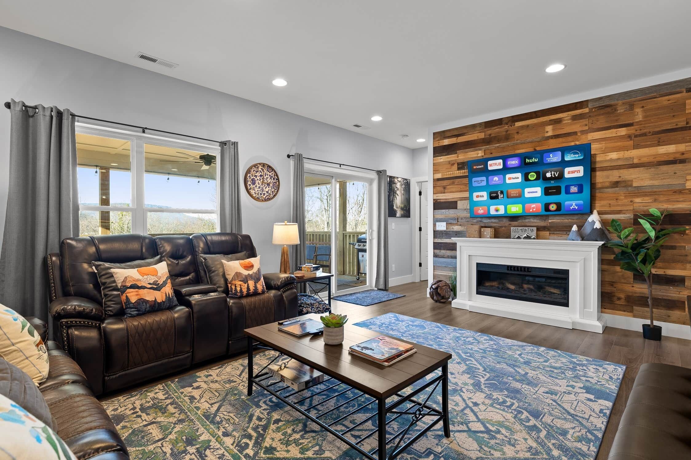 A modern living room with a leather sofa, a coffee table, and a flat-screen TV mounted on a wooden wall.