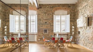 Una habitación amplia con pared de piedra, suelo de madera y un comedor con sillas coloridas y una mesa.