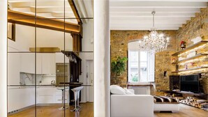 Eine moderne Küche mit weißen Schränken und einer Bar, ein Wohnzimmer mit weißem Sofa und Kamin, sowie eine Steinwand.