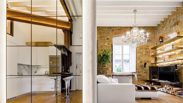 Una cocina moderna con gabinetes blancos y una barra, una sala de estar con un sofá blanco y una chimenea, y una pared de piedra.