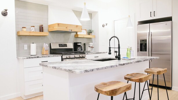 Eine moderne Küche mit weißen Schränken, einem Edelstahlkühlschrank, einem eingebauten Kochfeld und Holzbarhocker.
