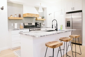 A modern kitchen with white cabinetry, a stainless steel refrigerator, a built-in stove, and wooden bar stools.