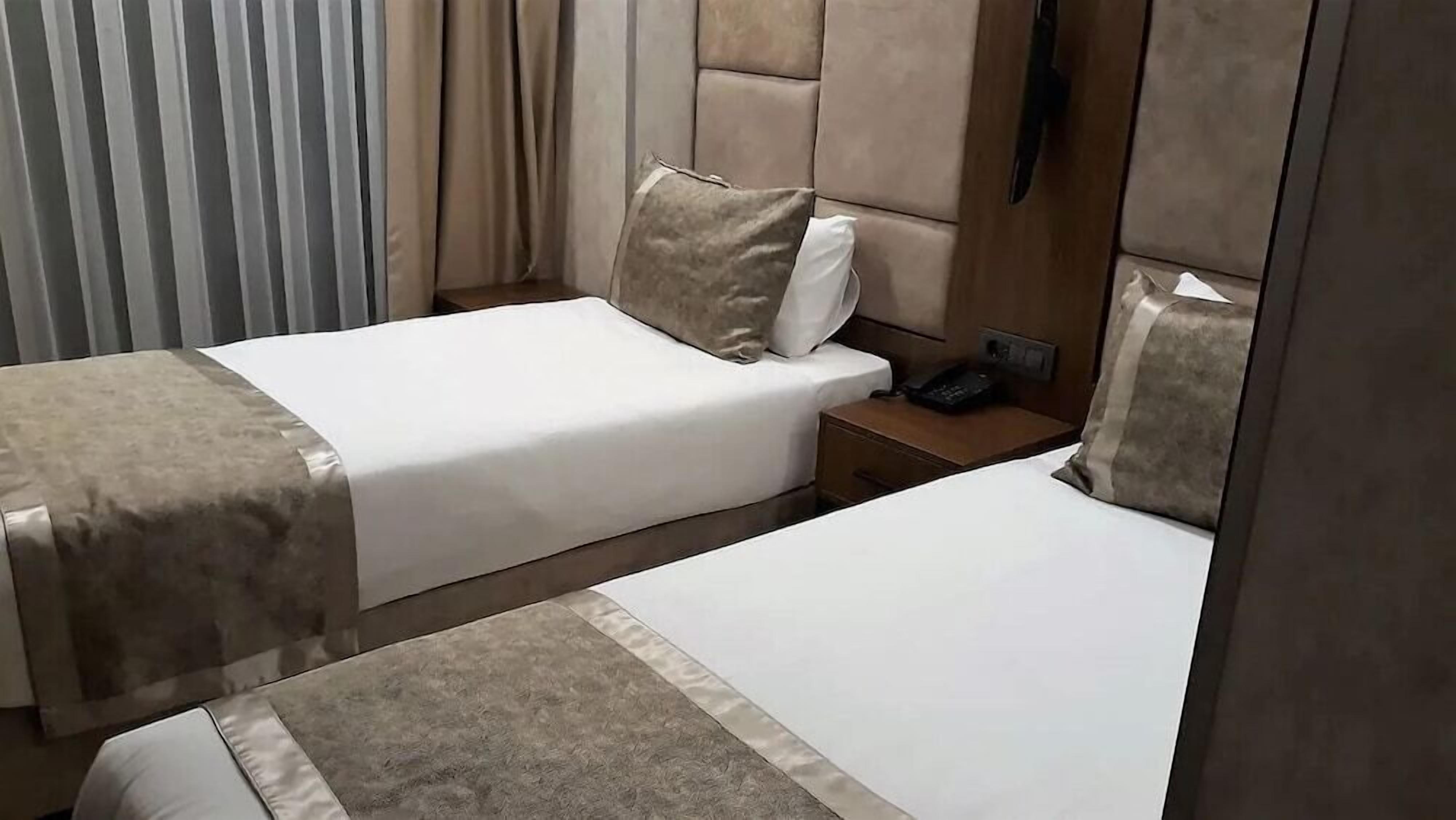 A hotel room with two beds, a nightstand, a telephone, and a window with blinds.