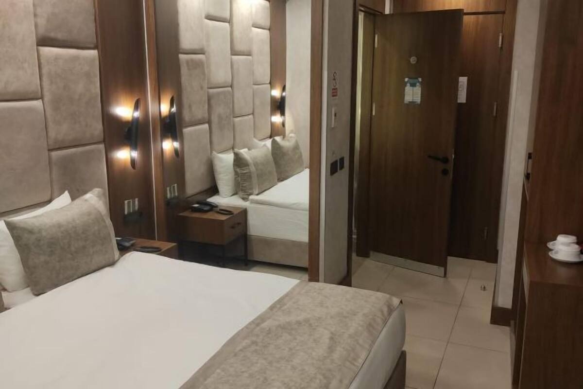 A hotel room with a large bed, a bedside table, a mirror, and a door leading to another room.