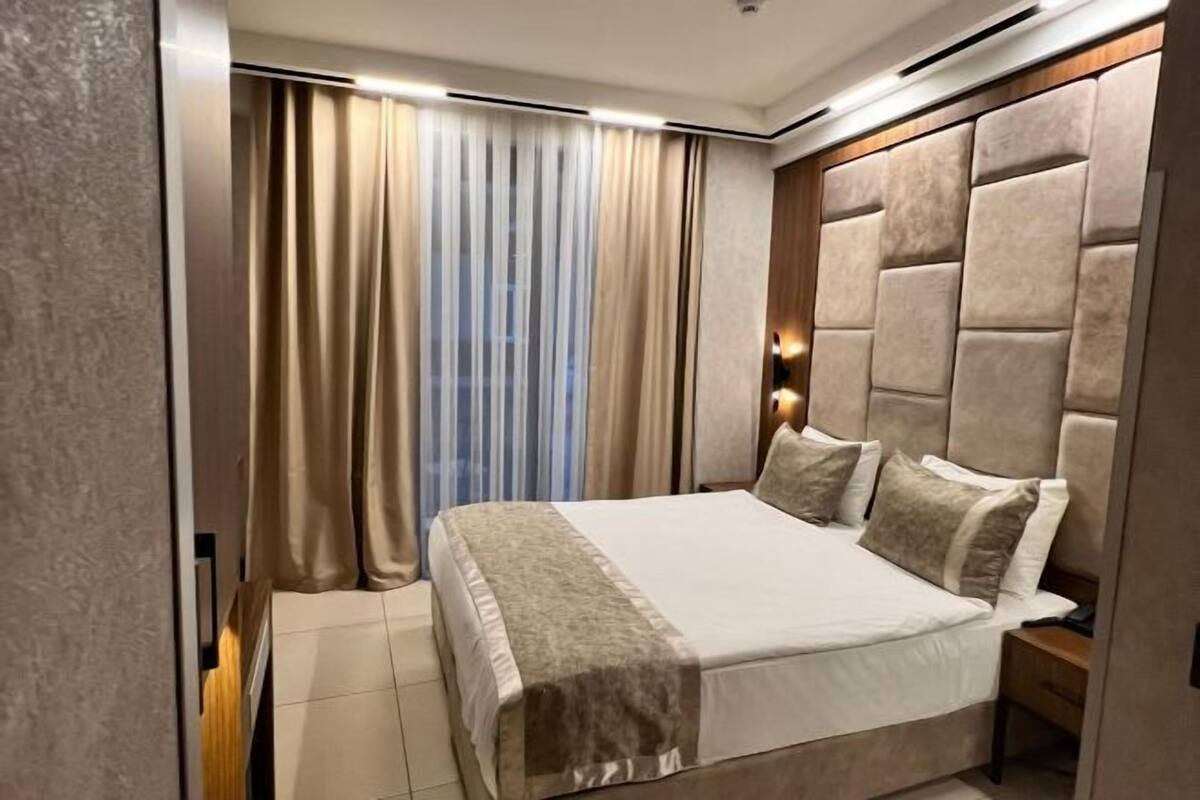 A bedroom with a large bed, a headboard, a nightstand, and a window with curtains.