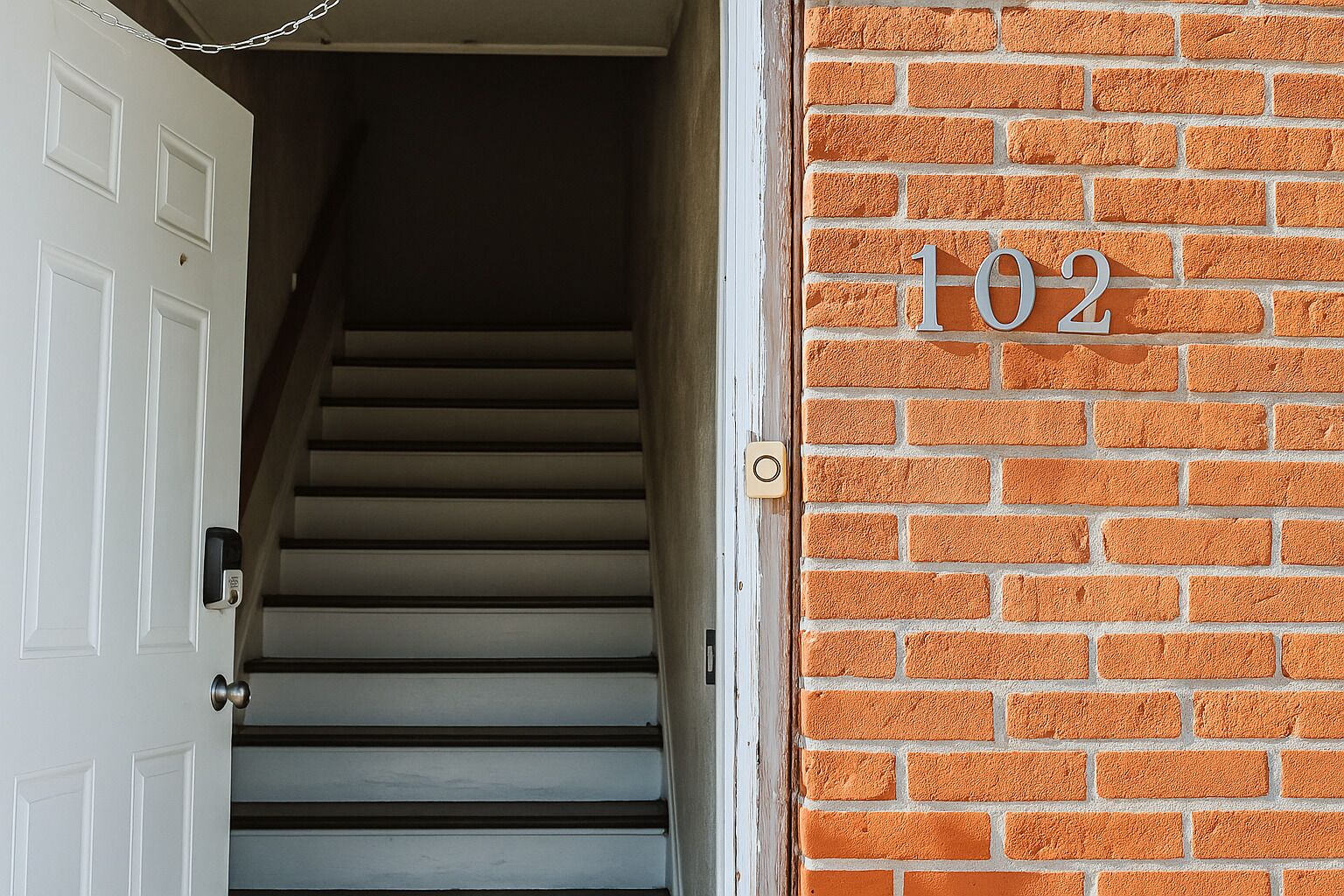 A staircase leading to a door with a number '102' on a brick wall.