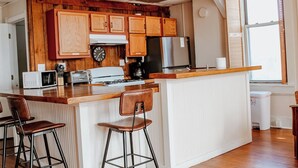 A kitchen with wooden cabinets, a central island with stools, a microwave, a stove, and a refrigerator. - 15% off Spring Special | Historic Bank | Wi-Fi | Close to Purdue (Oxford)