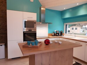 A modern kitchen with white cabinets, a stainless steel microwave, a built-in oven, a coffee maker, and a window with a view of a house.