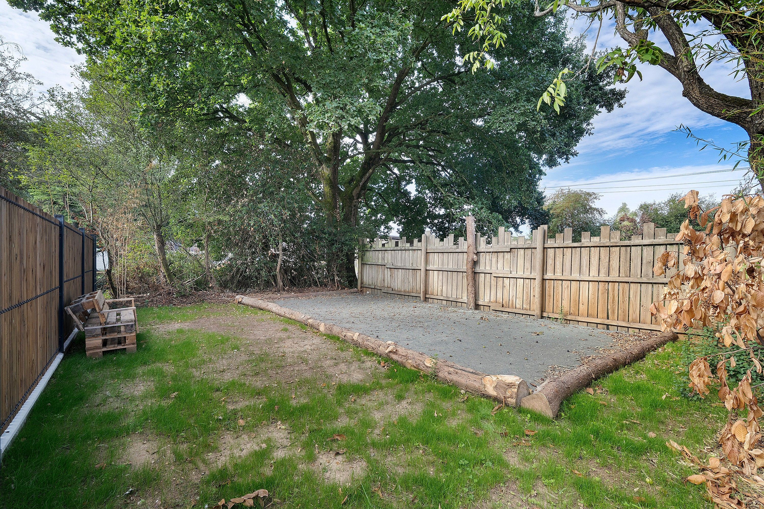 Un patio trasero cercado con zona de grava, valla de madera y un árbol.