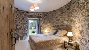 Ein Schlafzimmer mit einer Steinsandsteinwand, einem Bett mit einem gemusterten Bettbezug, einer Nachttischlampe und einem Sessel.