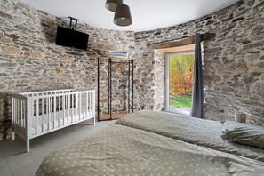Ein Schlafzimmer mit Steinwänden, einem Kinderbett, einem Bett mit Punkten und einem Hängesessel, sowie einem an der Wand befestigten Fernseher.