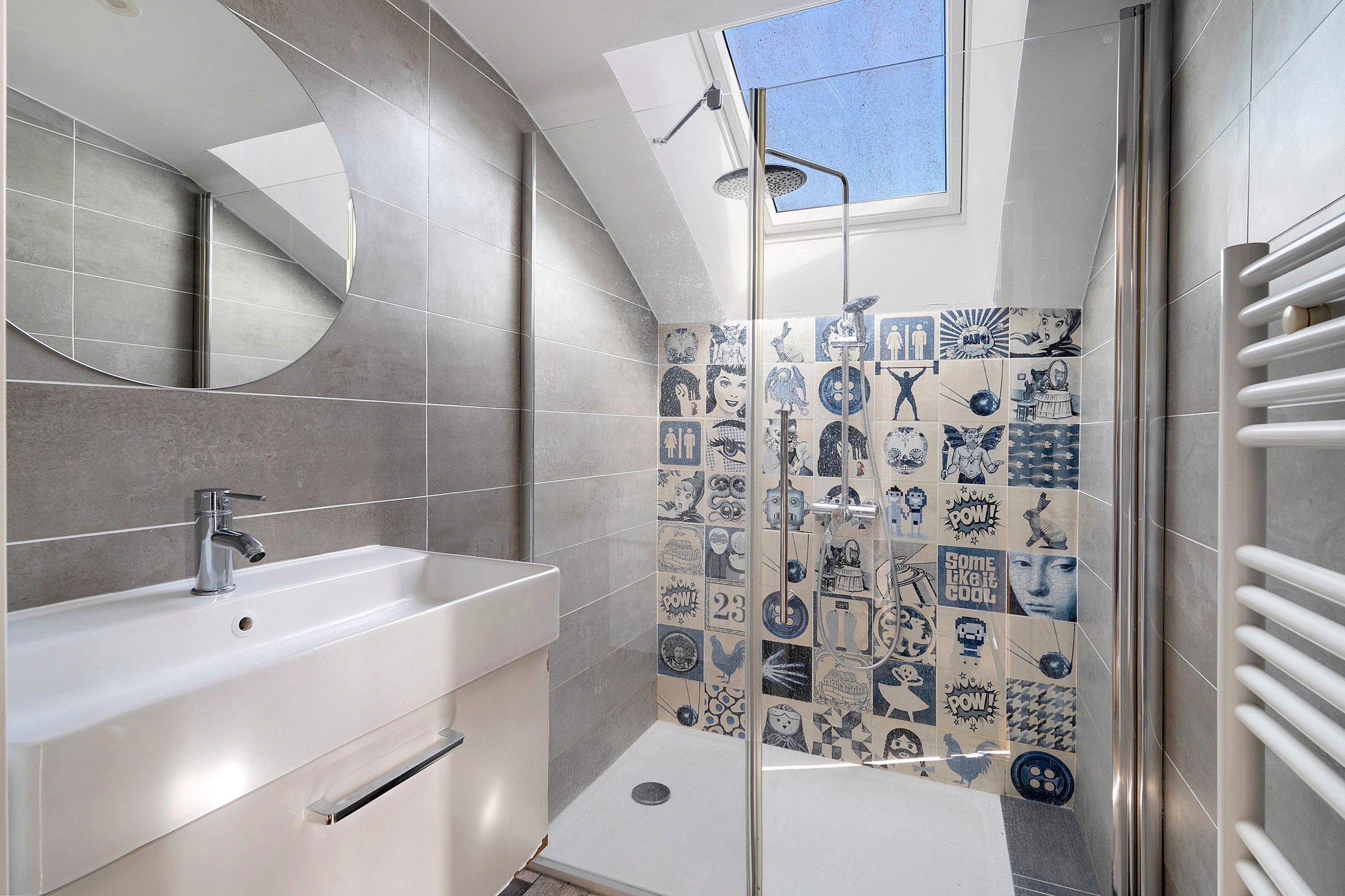 Une salle de bain moderne avec un lavabo blanc, une douche dotée d’une porte en verre et un puits de lumière.