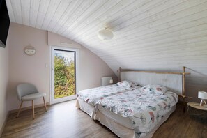 A bedroom with a sloped ceiling, a bed with floral bedding, a chair, and a view through a door.