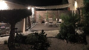 Een terras buiten met een tafel en stoelen, omgeven door planten en een houten hek.