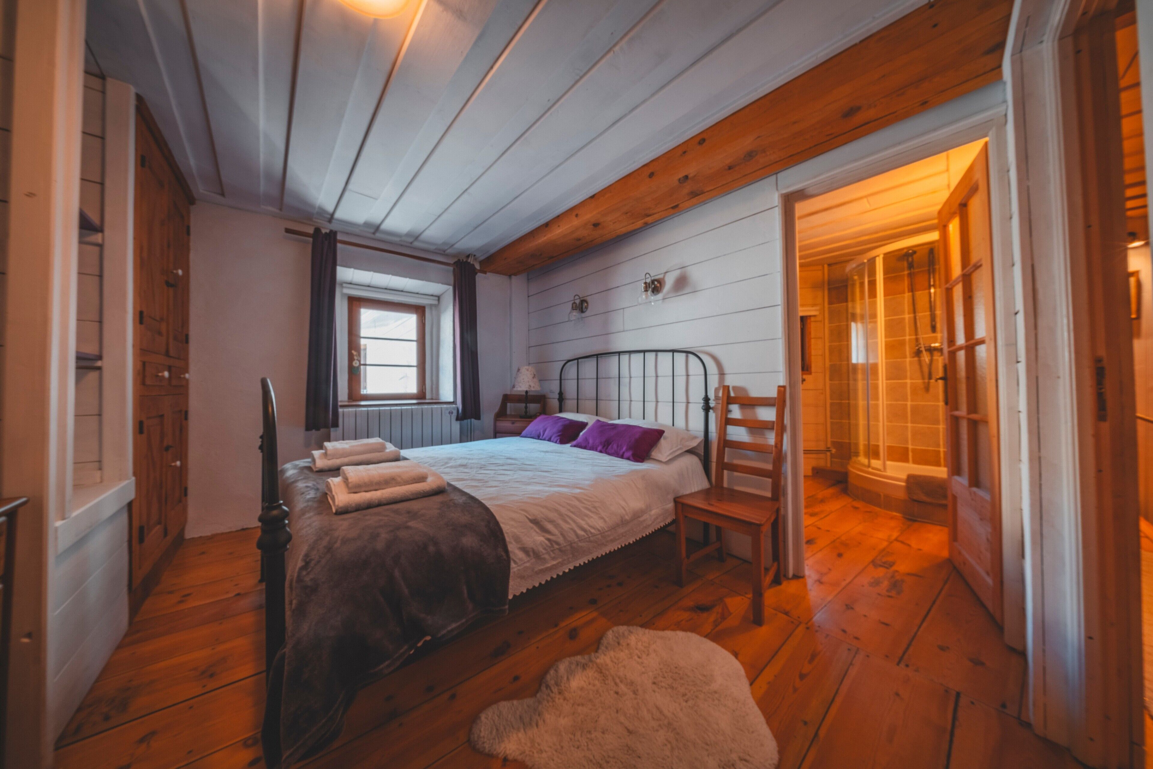 Una camera da letto con pavimento in legno, un letto con testiera, una finestra e una porta che dà su un bagno.