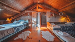 Une chambre mansardée chaleureuse avec des poutres apparentes, deux lits, un plancher en bois et une petite table.
