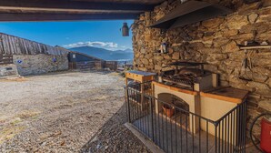Un espace cuisine extérieur doté de murs en pierre, d’un plafond en bois et offrant une vue sur les montagnes.
