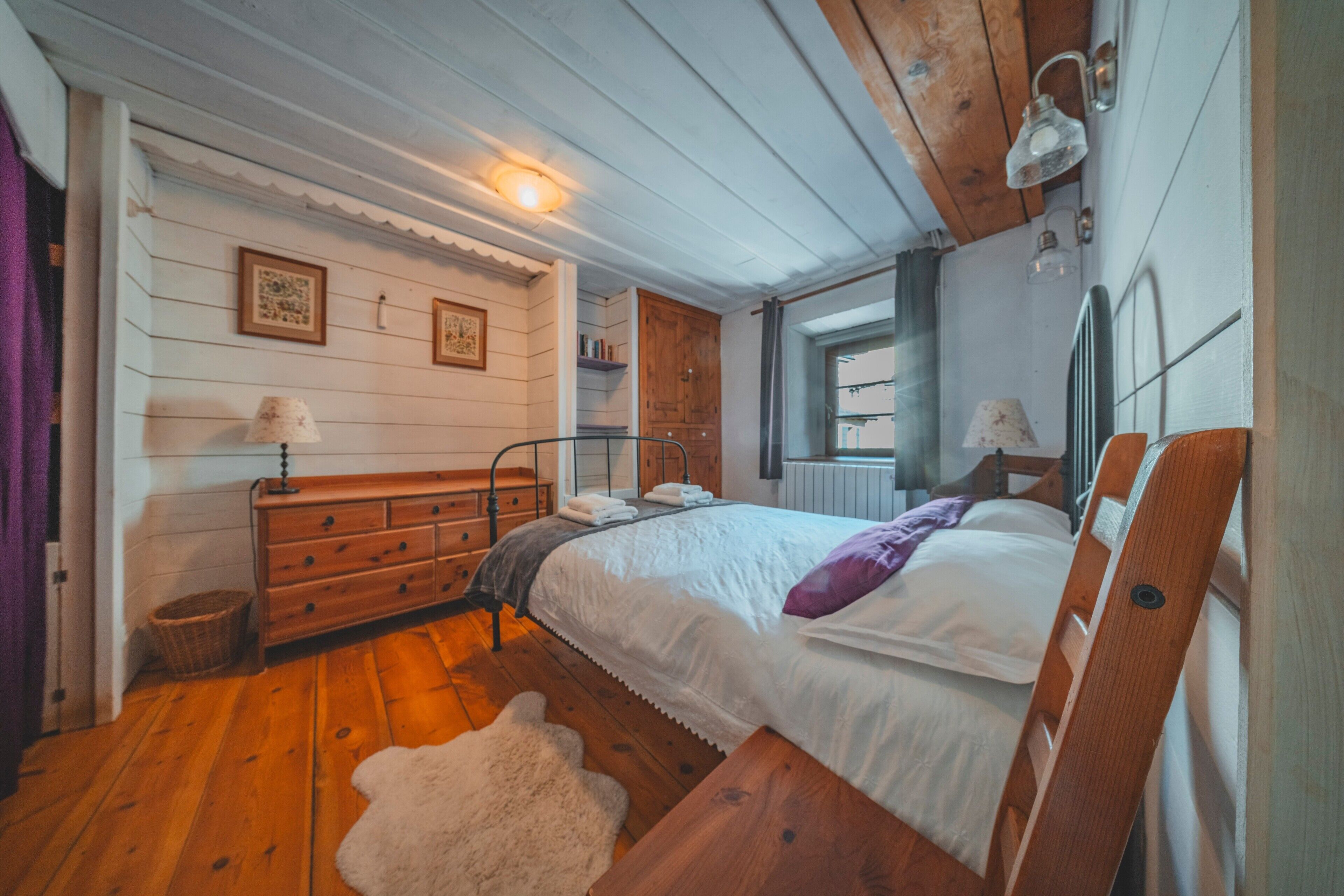 A bedroom with a wooden bed, a dresser, a lamp, and a window.