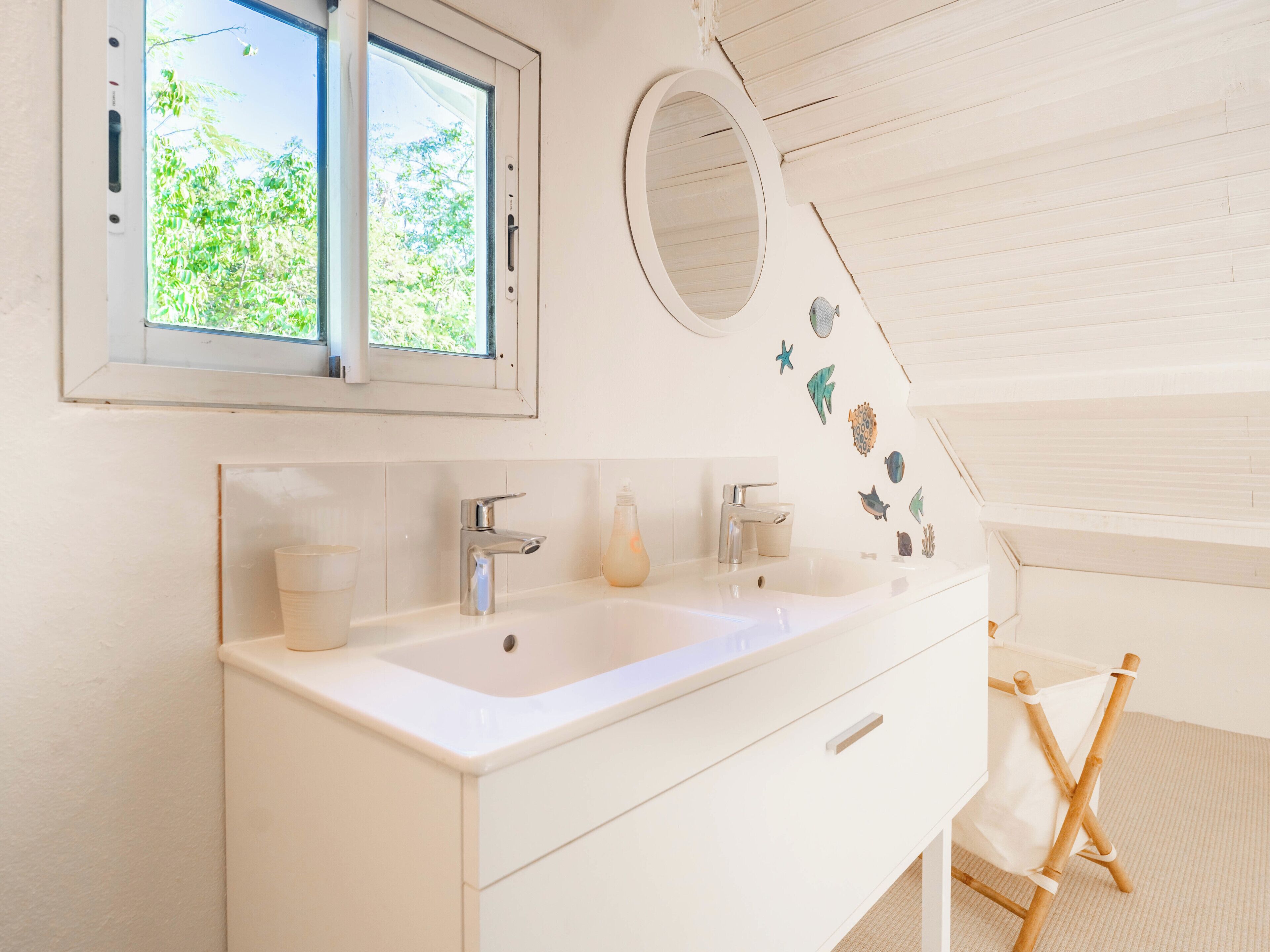 Une salle de bain avec un meuble-lavabo blanc, un grand miroir et une fenêtre donnant sur un paysage verdoyant.