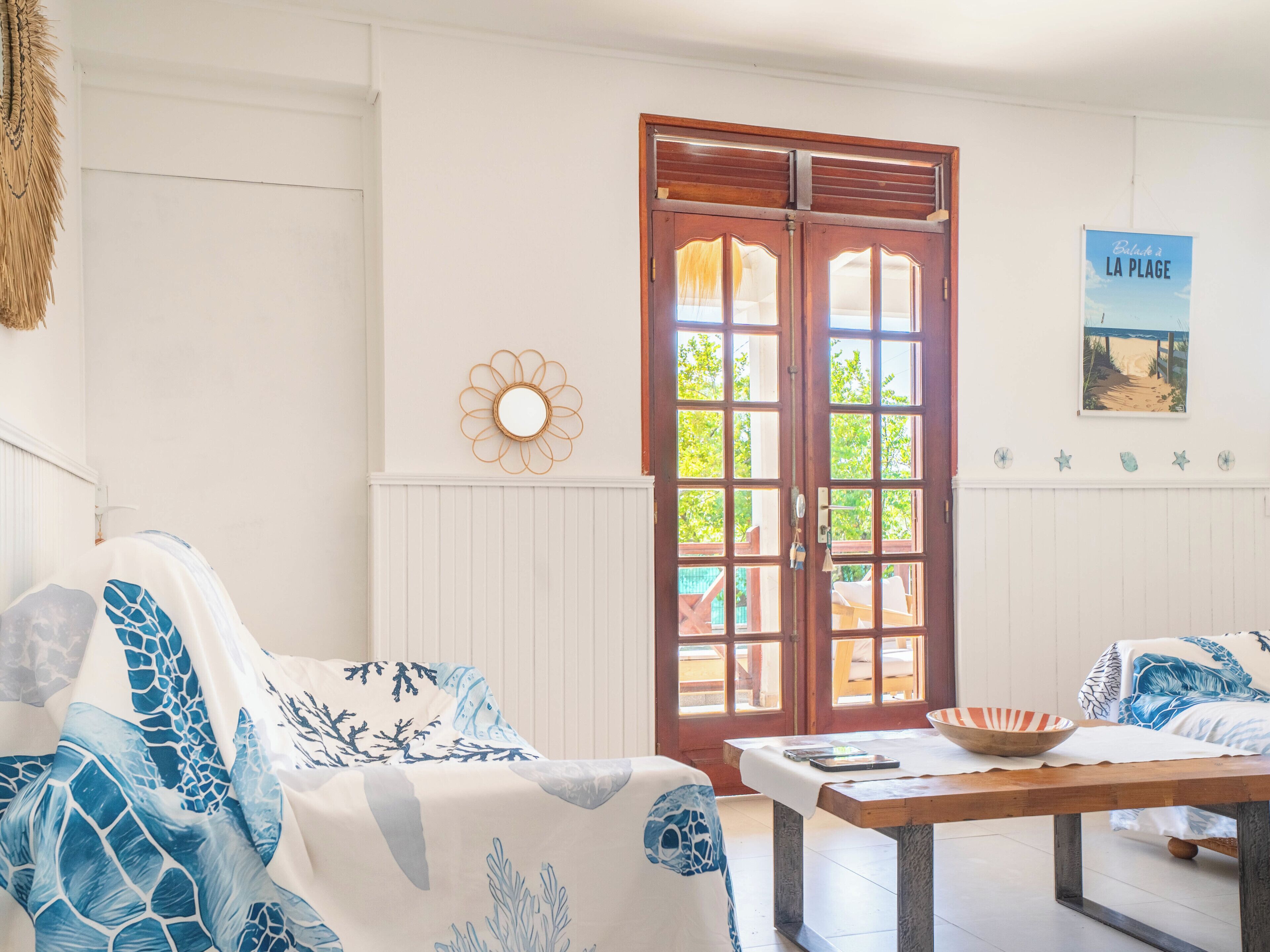 A room with a wooden door, a white wall with a poster, a round mirror, and a table with a bowl.
