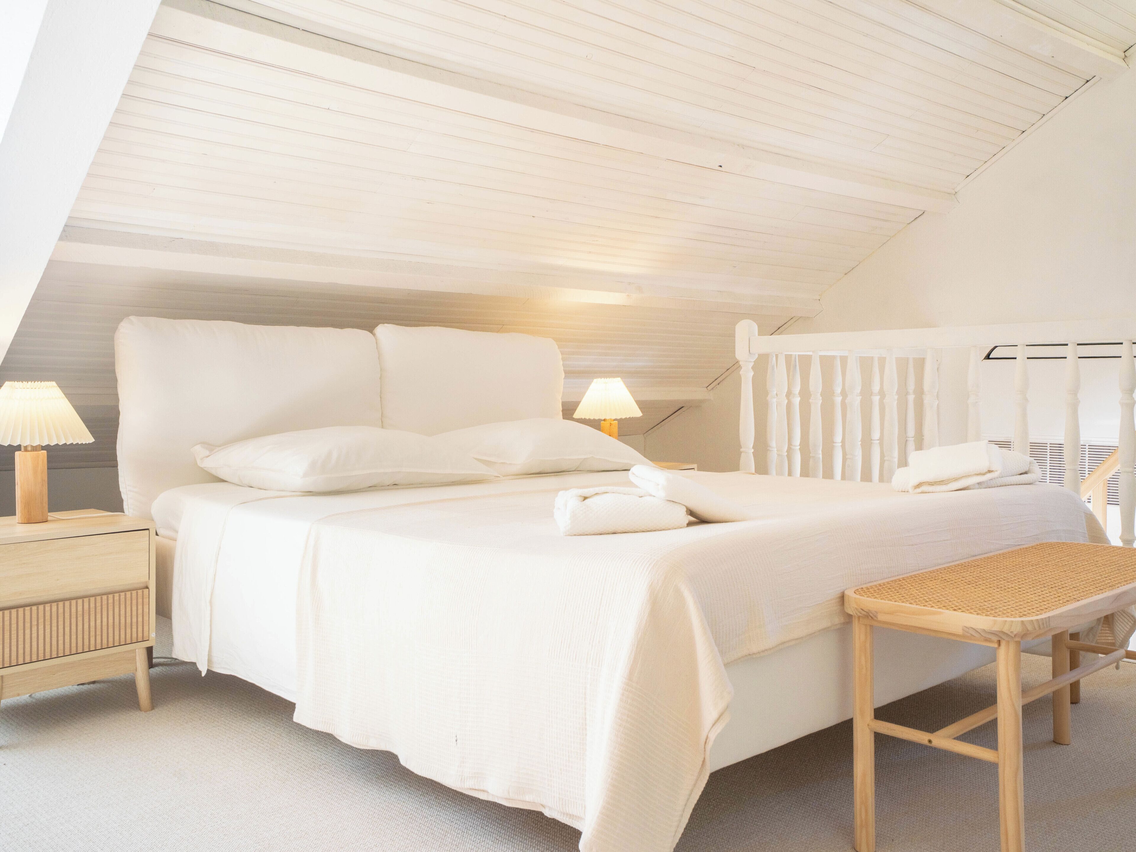 Ein Schlafzimmer mit einem großen Bett, zwei Nachttischen, einer hölzernen Bank und einer geneigten Decke.