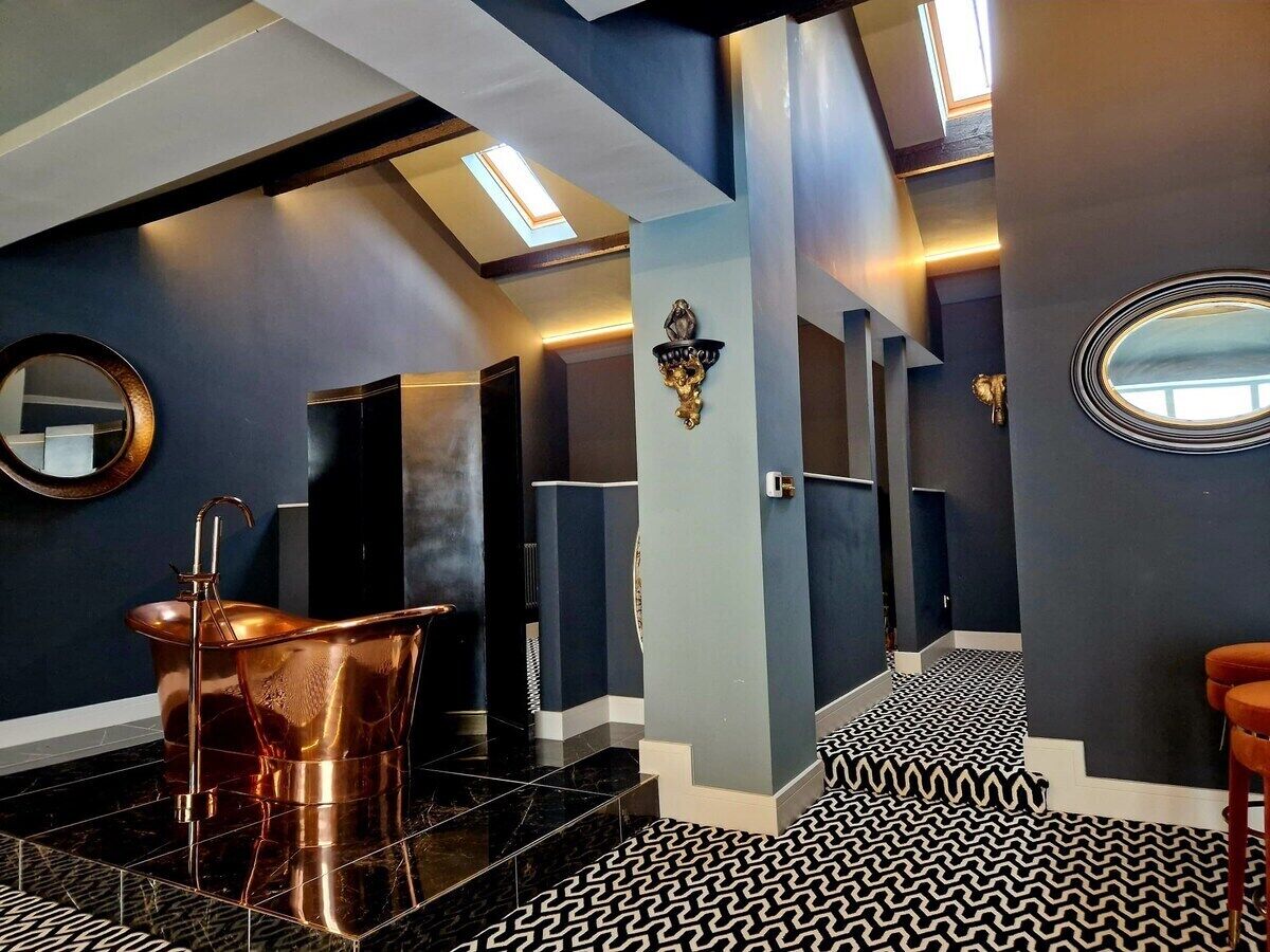 Een moderne badkamer met een koperen bad, vloer met zwart-wit patroon en een dakraam.