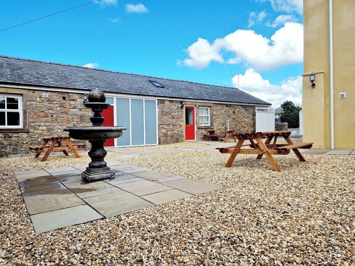 A stone building with a red door, a fountain, and picnic tables.