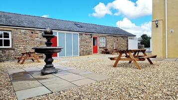 A stone building with a red door, a fountain, and picnic tables.
