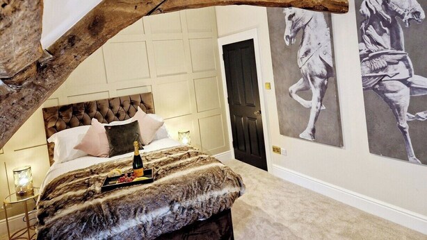 A bedroom with a large bed, a wooden ceiling beam, and two wall-mounted paintings of horses.