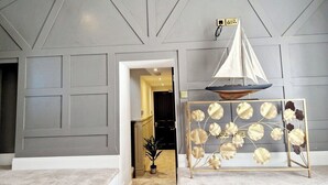 A hallway with a grey wall, a small potted plant, and a decorative sailboat model on a stand.