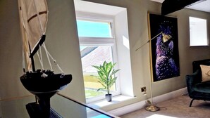 A room with a large window, a potted plant, a modern lamp, and a dark-colored chair.