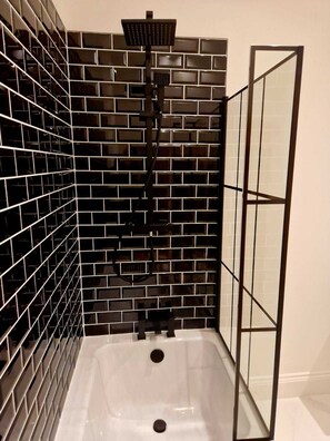 Un baño con paredes de azulejos blancos y negros, una bañera blanca y una mampara de ducha de vidrio.
