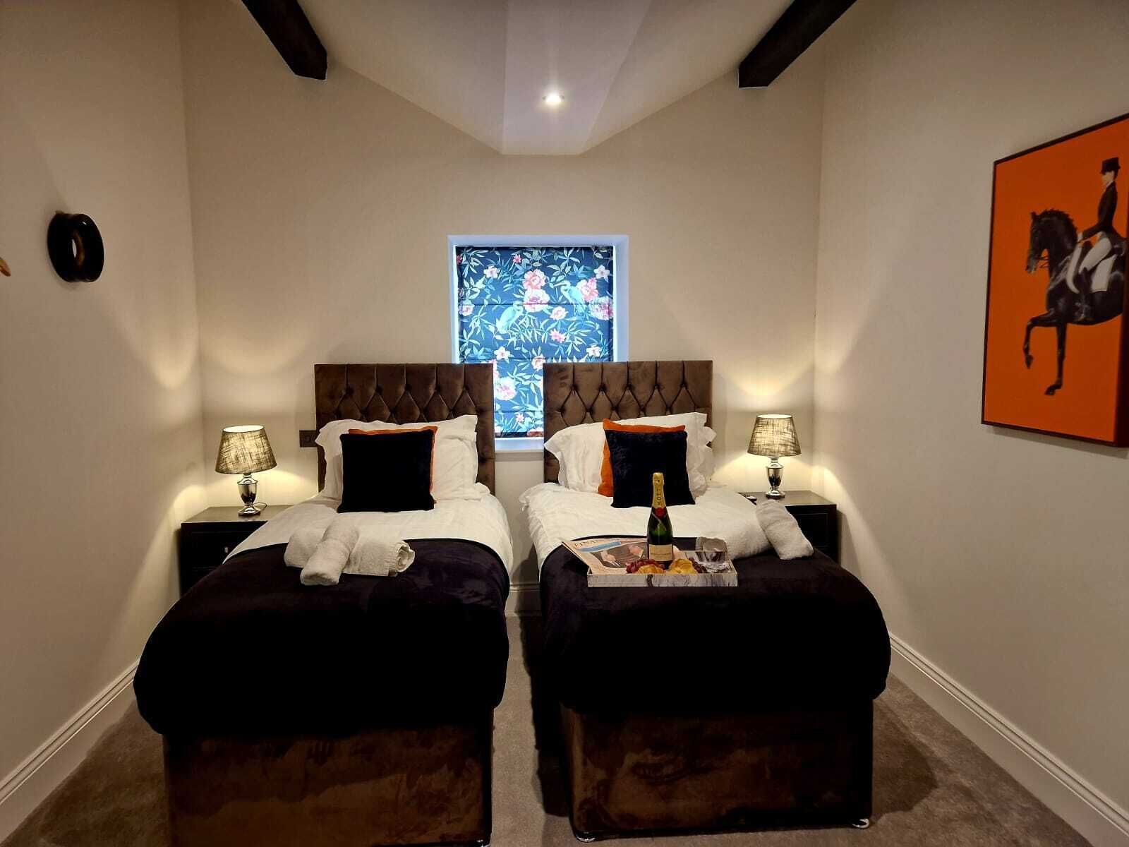 Habitación de hotel con dos camas, una ventana que da a un jardín floral, una obra de arte enmarcada en la pared y una botella de champán sobre la mesita de noche.