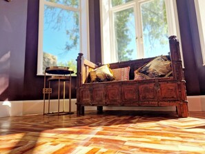 Un banc en bois avec des coussins, un petit tabouret et un sol à motifs.