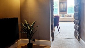 A hallway with a potted plant, a radiator, and a stone wall leading to a living area with a sofa and a chandelier. - The Hamilton luxury apartments-Lord William suite (Cabus)