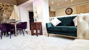 A modern living room with a green sofa, purple chairs, a wooden coffee table, and a stone wall. - The Hamilton luxury apartments-Lord William suite (Cabus)