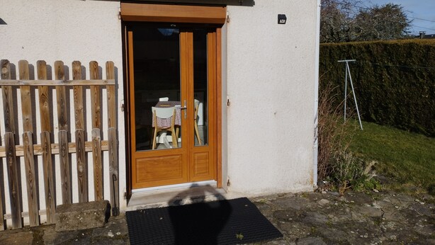 Una puerta de madera con un panel de vidrio, un escalón que lleva a la puerta, y una cerca de madera a la izquierda.
