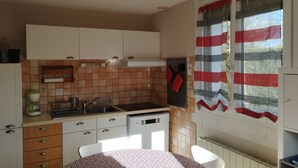 Una cocina compacta con armarios blancos, un salpicadero azulejado, un lavamanos y una ventana con cortinas rojas.